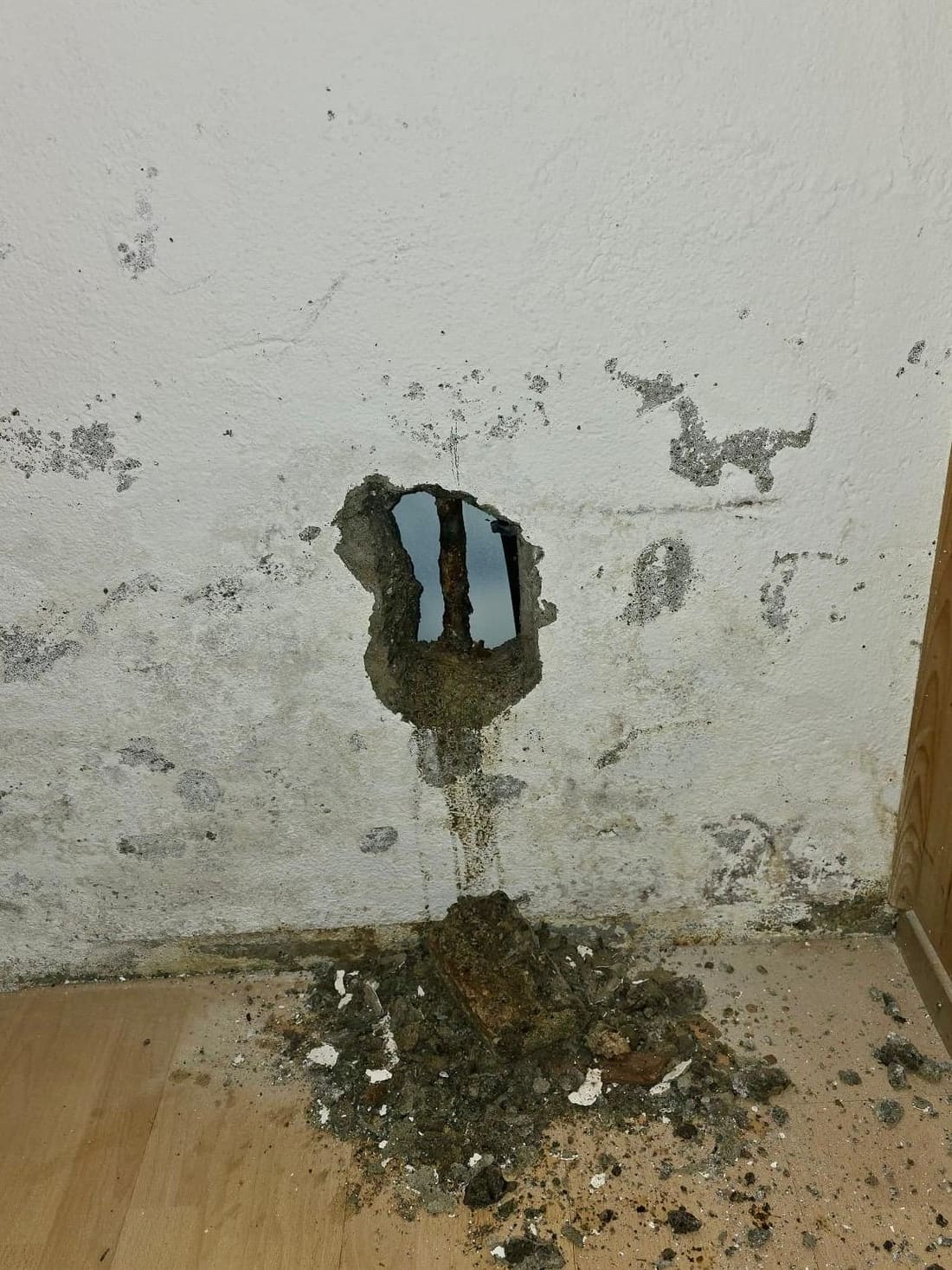 Mur ouvert sur le tuyau d’eau chaude corrodé, traces d’humidité tout autour